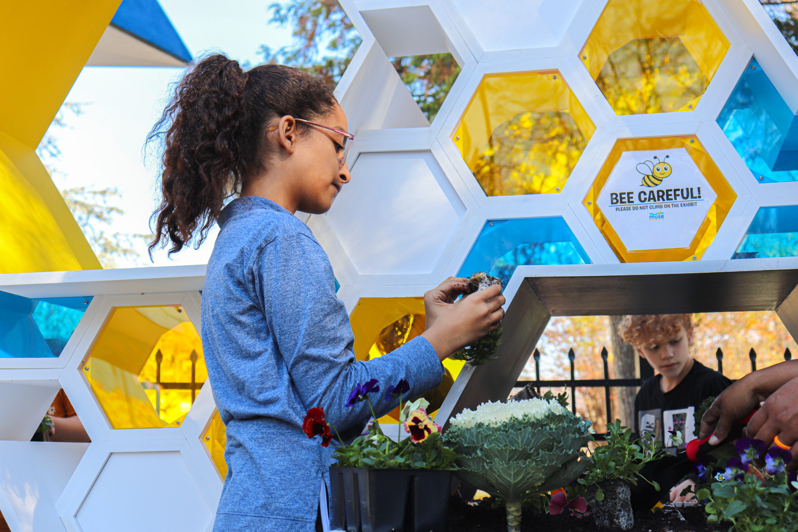 A young girl in glasses helps plant flowers outside